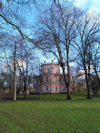 Haus Greiffenhorst zwischen kahlen Bäumen. Grünes Gras, blauer Himmel