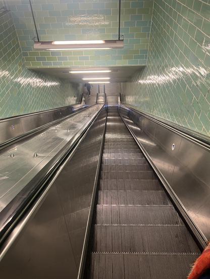 Foto, Blick die Rolltreppe abwärts in eine U-Bahn Station. Die Wände sind grün gekachelt.