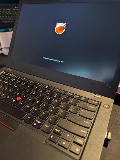 Closer view of the ThinkPad T480 boot screen showing the red FreeBSD orb logo above the text ‚To interrupt normal startup, press Enter‘, with the keyboard and red TrackPoint in the foreground.
