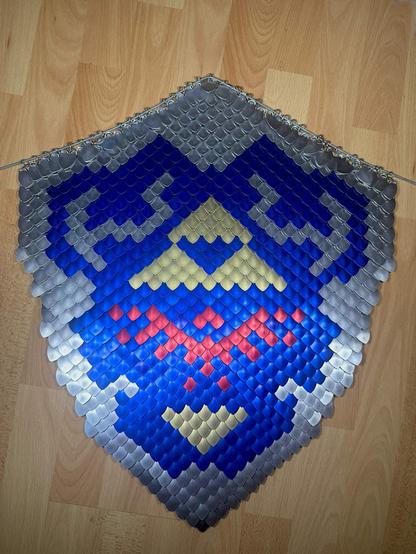 real sized shield made of dragon/fish scale like metal plates, all tiny and overlapping to create a large image of the Hylian Shield from Ocarina of Time.