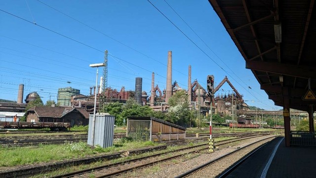 Ein altes Stahlwerk mit Schornsteinen, dahinter blauer Himmel.